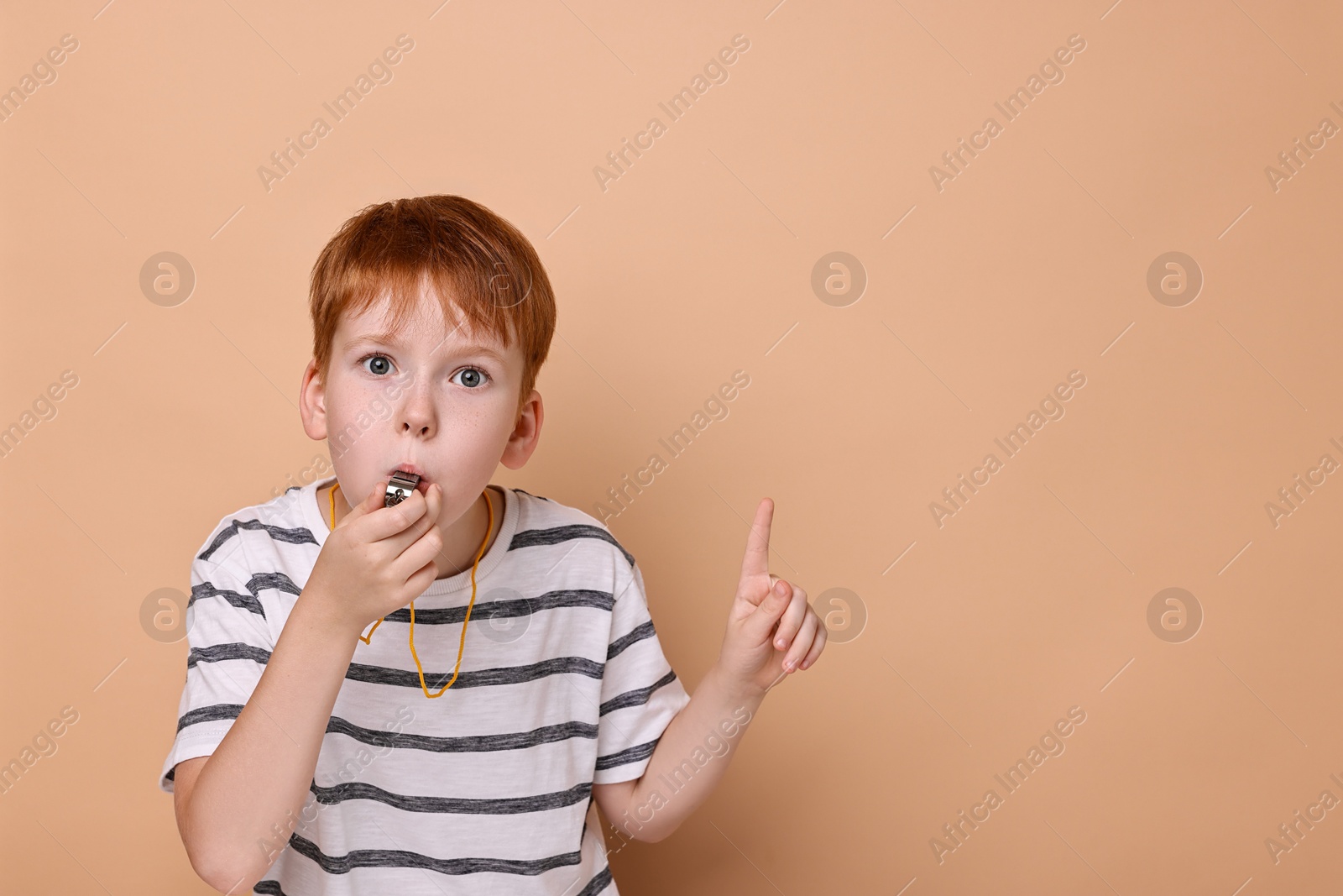 Photo of Little boy blowing whistle on beige background, space for text