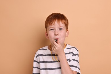 Little boy blowing whistle on beige background