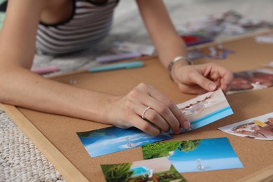 Photo of Creating vision board. Woman pinning photo to corkboard on floor indoors, closeup