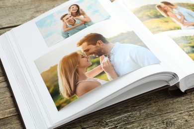 Photo of Different photos in open photo album on wooden table, closeup