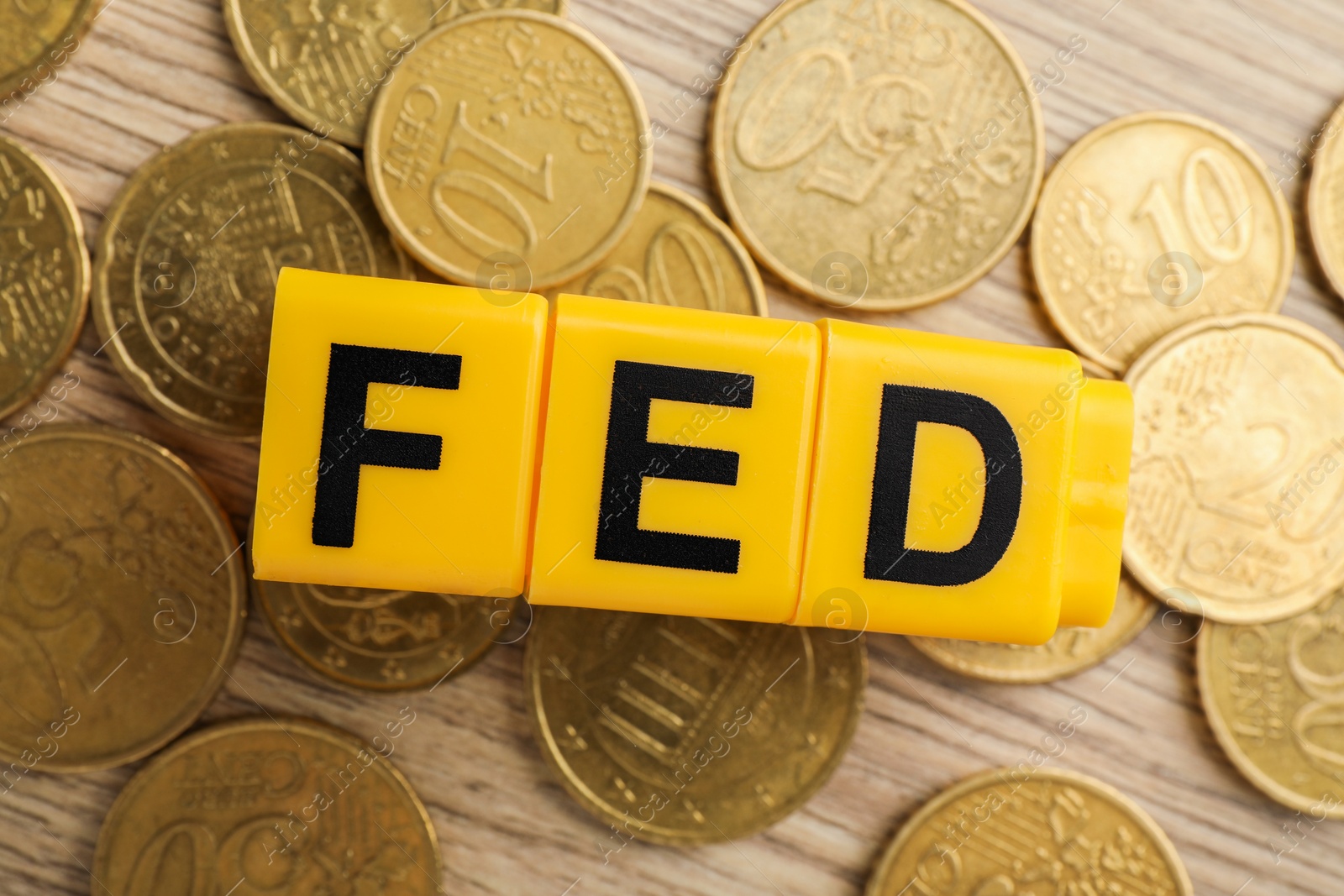 Photo of Cubes with letters Fed (Federal Reserve System) and coins on wooden table, flat lay