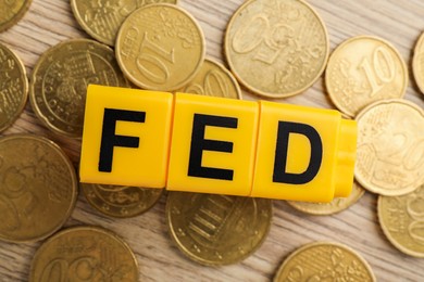 Photo of Cubes with letters Fed (Federal Reserve System) and coins on wooden table, flat lay