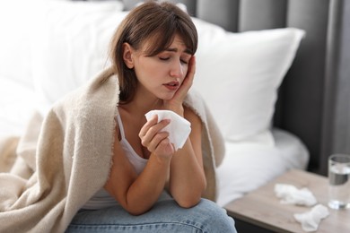 Woman wrapped in blanket suffering from sinusitis at home