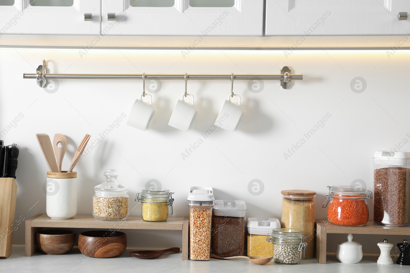 Photo of Different types of cereals and legumes in containers on light marble table in kitchen