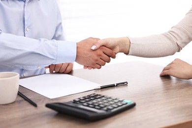 Photo of Banker and client shaking hands at table in office, closeup