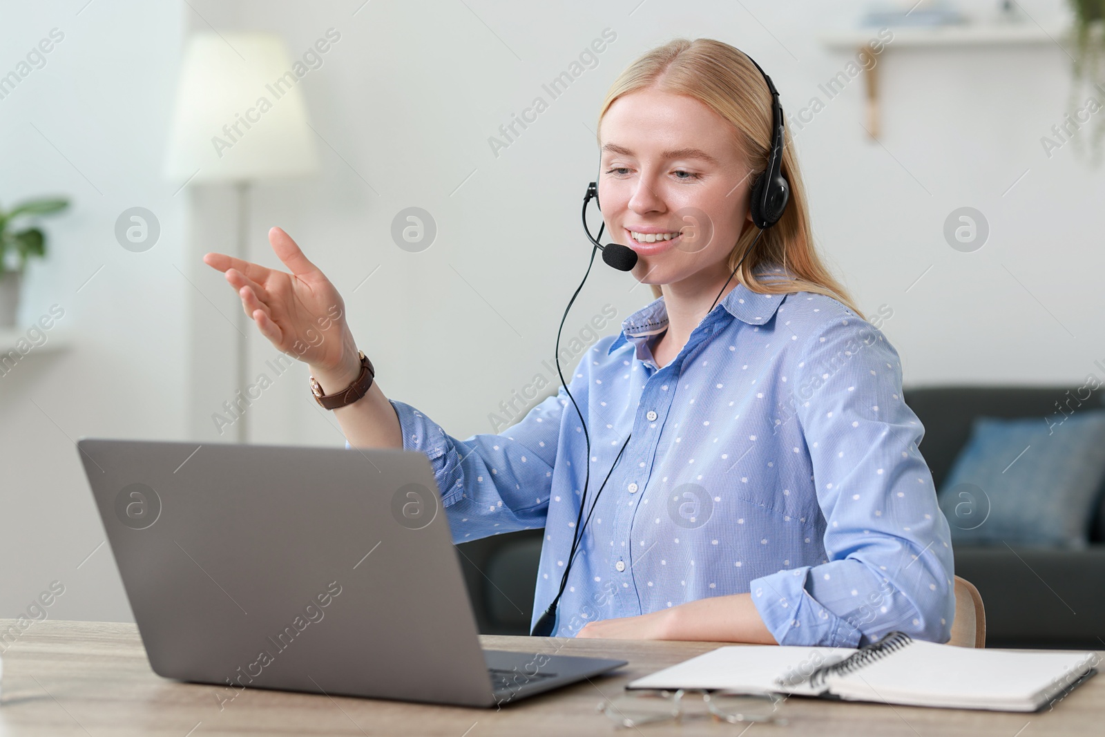 Photo of Interpreter in headset having video chat via laptop at table indoors