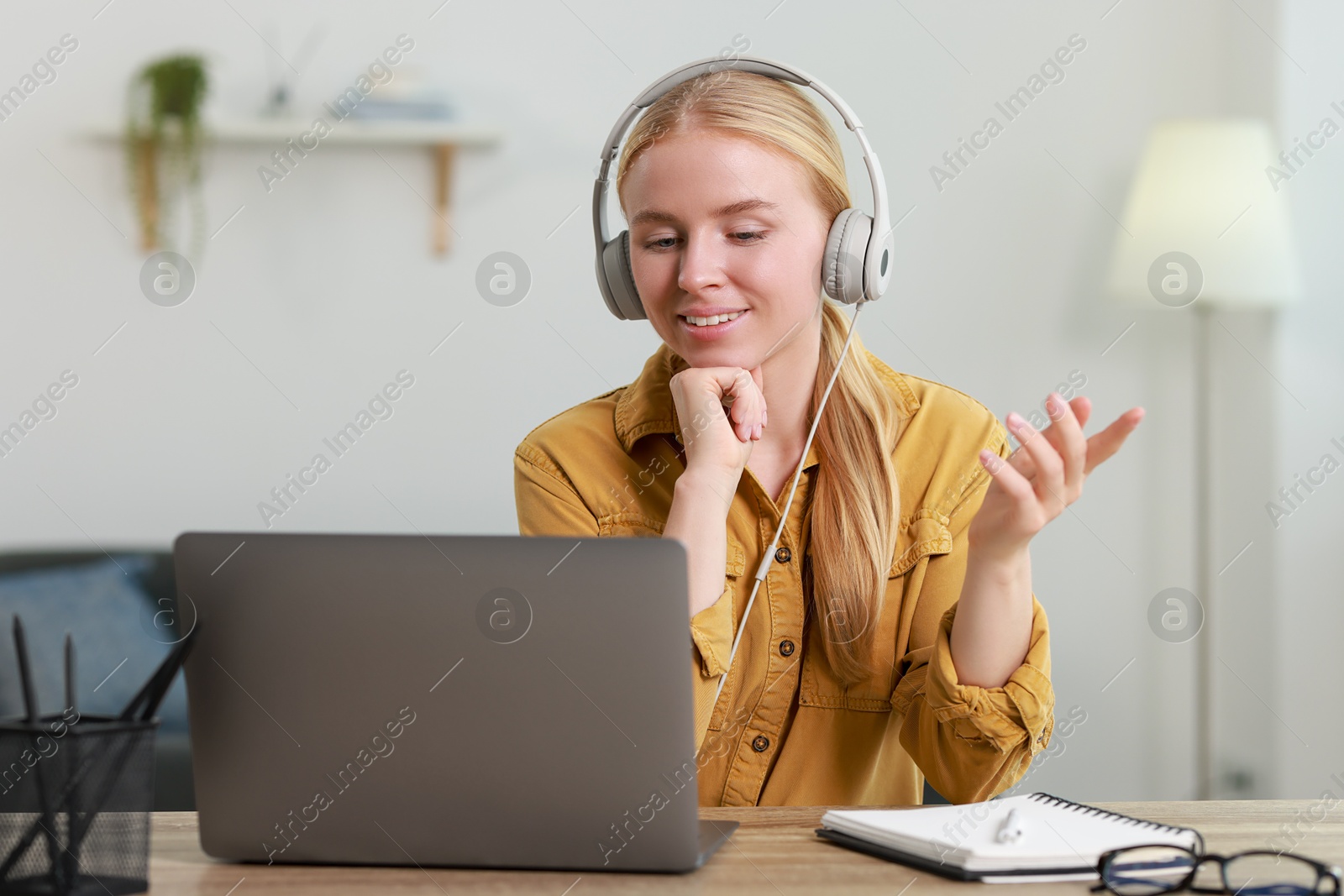 Photo of Interpreter in headphones having video chat via laptop at table indoors