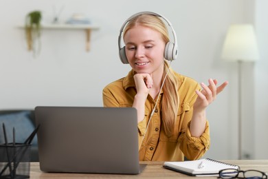 Photo of Interpreter in headphones having video chat via laptop at table indoors