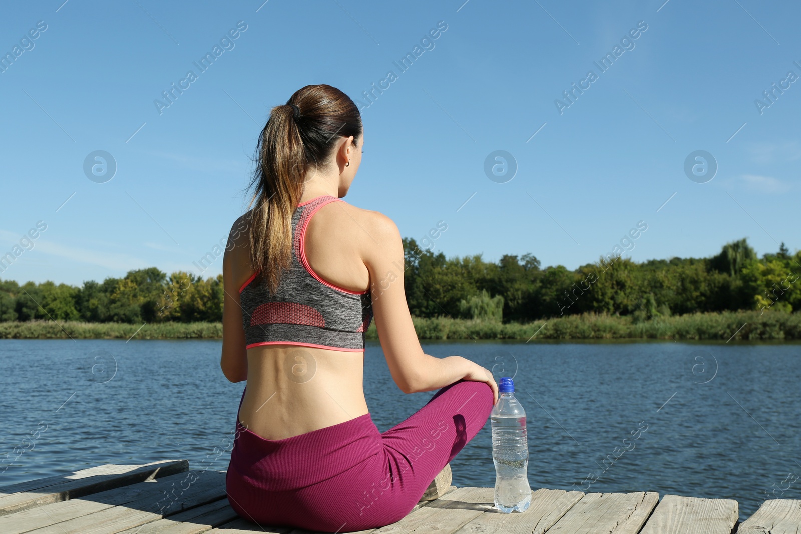 Photo of Woman with bottle of soda water near lake, back view