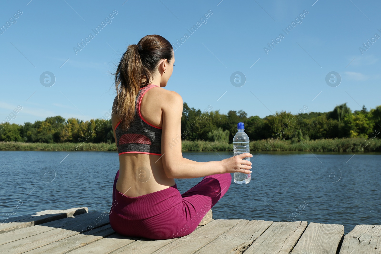 Photo of Woman with bottle of soda water near lake, back view