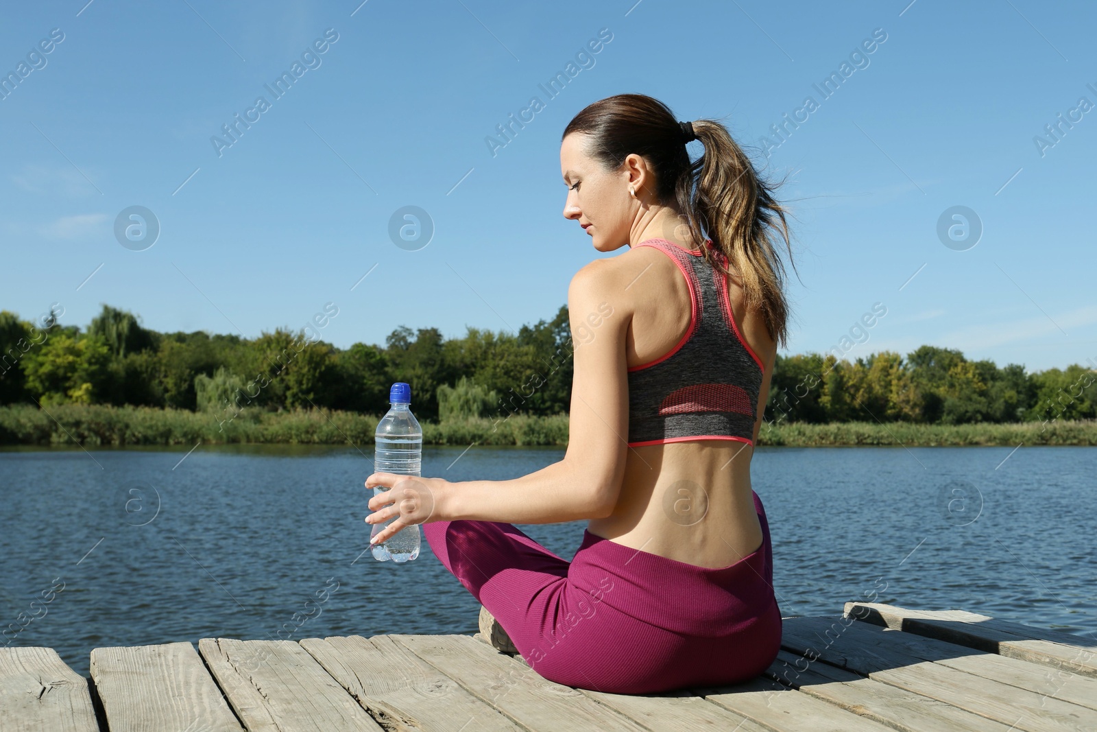 Photo of Woman with bottle of soda water near lake, back view