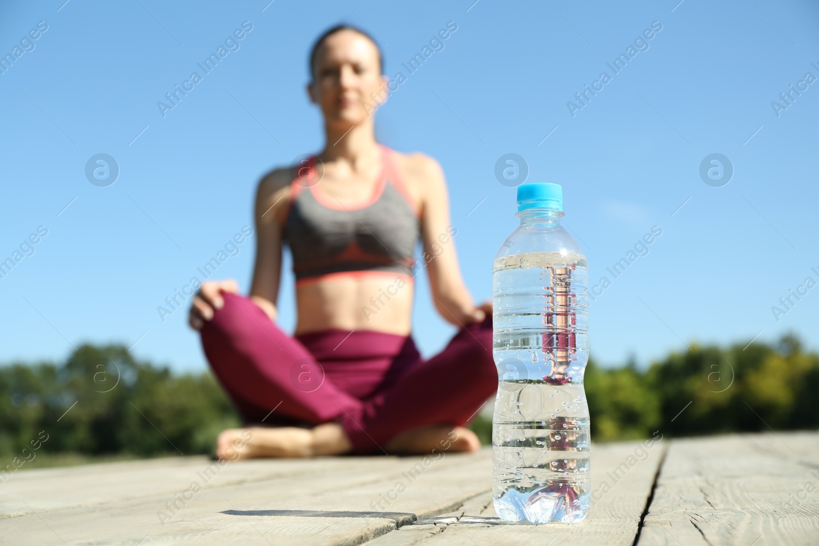 Photo of Woman sitting on wooden deck outdoors, focus on bottle of soda water