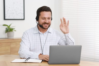 Interpreter in headset having video chat via laptop at wooden table indoors