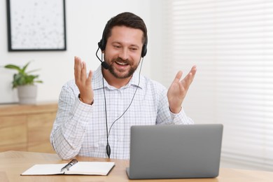 Photo of Interpreter in headset having video chat via laptop at wooden table indoors