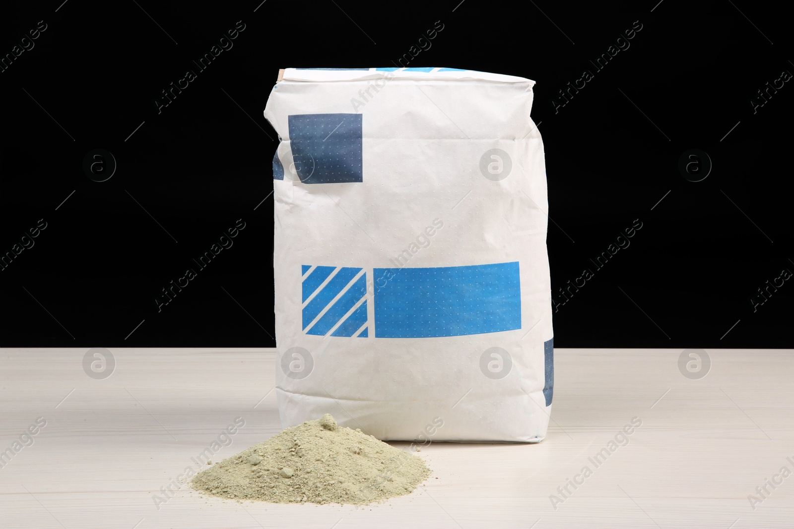 Photo of Bag of cement on light wooden table against black background. Building material