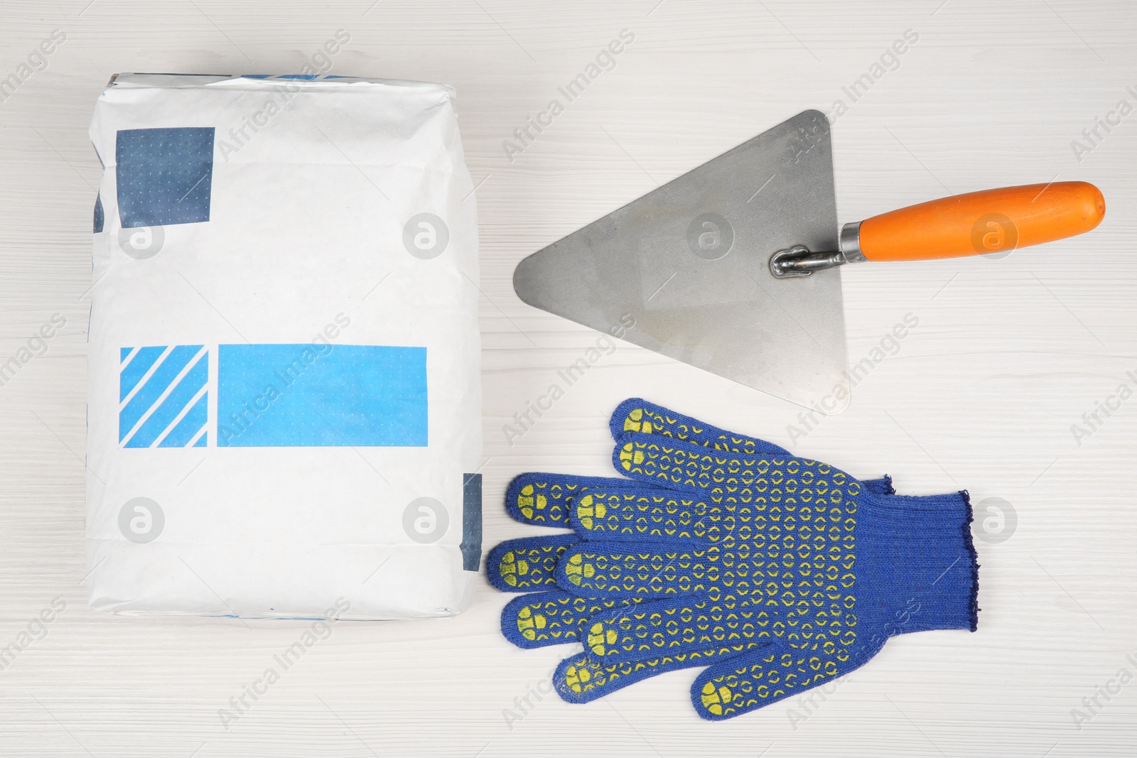 Photo of Bag of cement powder, putty knife and rubber gloves on light wooden table, flat lay. Building material