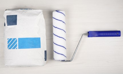 Bag of cement powder, and paint roller on light wooden table, flat lay. Building material