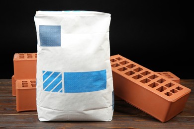 Photo of Red bricks and bag of cement powder on wooden table. Building materials