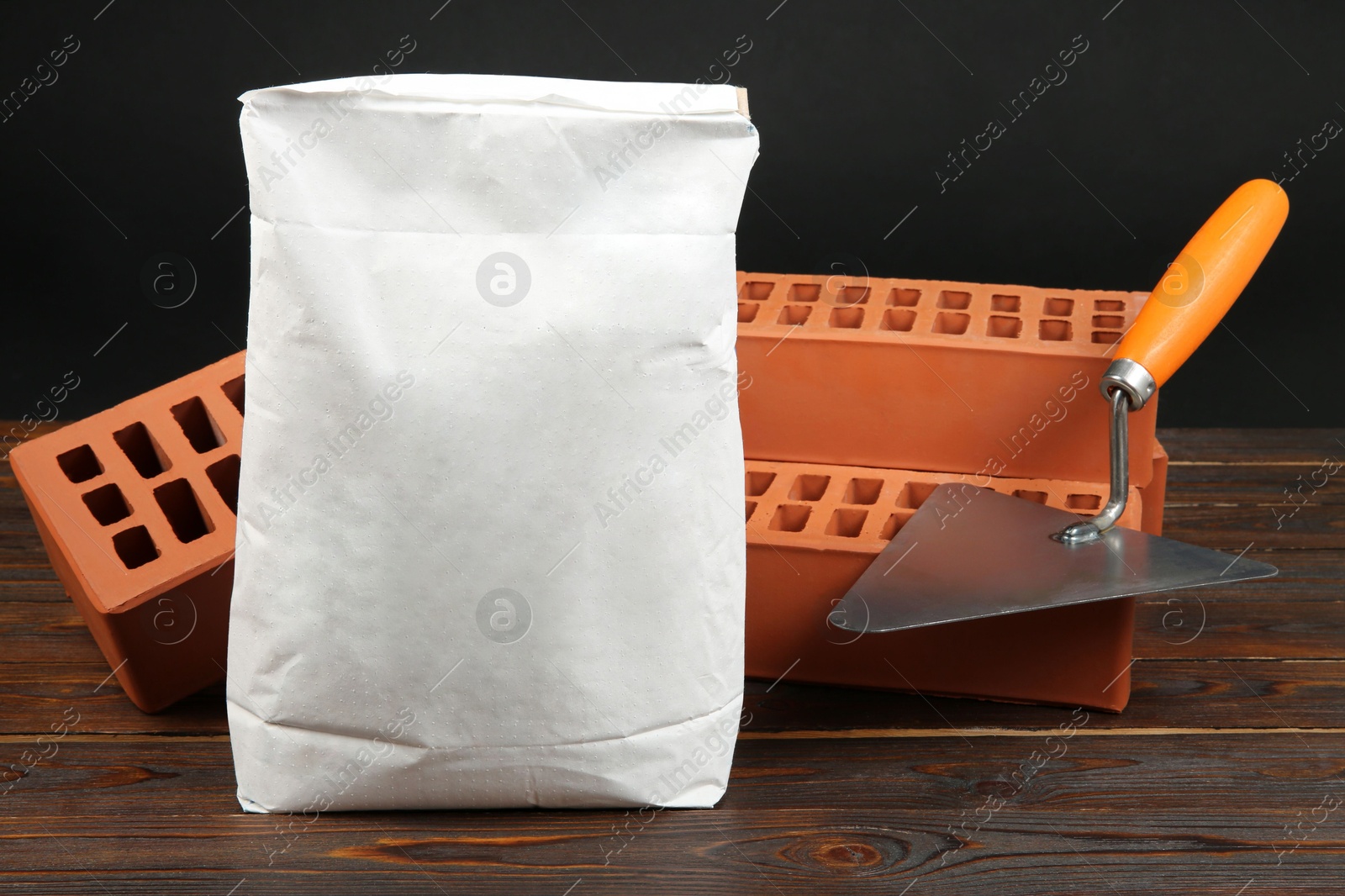 Photo of Red bricks, bag of cement powder and putty knife on wooden table. Building materials