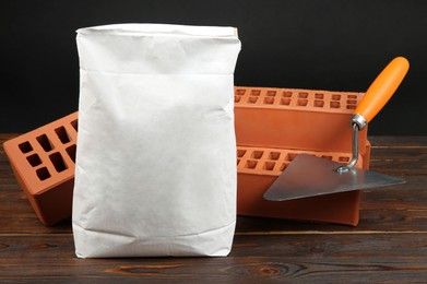 Red bricks, bag of cement powder and putty knife on wooden table. Building materials