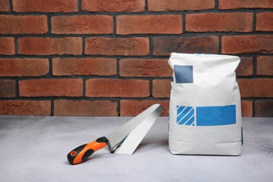 Photo of Bag of cement and trowel on light textured table against red brick wall. Space for text