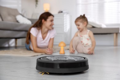 Photo of Mother spending time with her daughter in room, focus on robotic vacuum cleaner