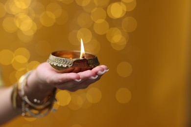 Photo of Diwali celebration. Woman holding lit diya lamp on color background with blurred lights, closeup. Space for text