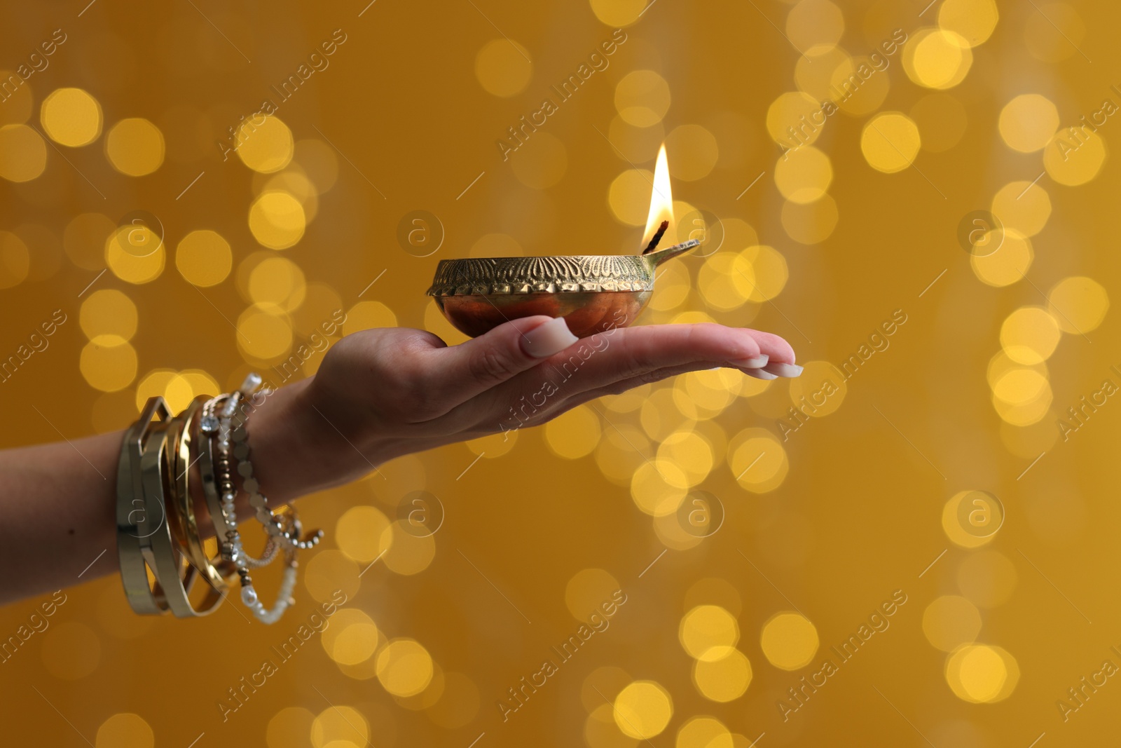 Photo of Diwali celebration. Woman holding lit diya lamp on color background with blurred lights, closeup