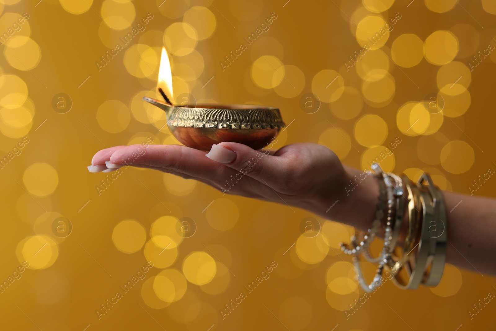 Photo of Diwali celebration. Woman holding lit diya lamp on color background with blurred lights, closeup