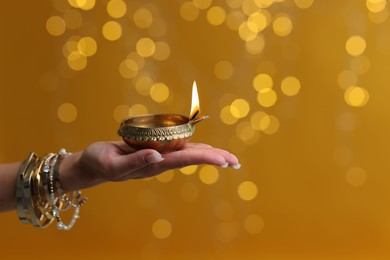 Photo of Diwali celebration. Woman holding lit diya lamp on color background with blurred lights, closeup. Space for text