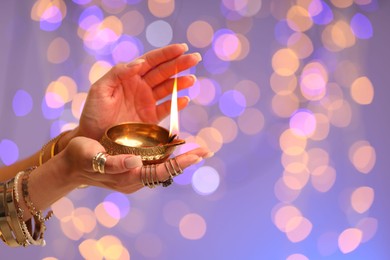 Photo of Diwali celebration. Woman holding lit diya lamp on color background with blurred lights, closeup. Space for text