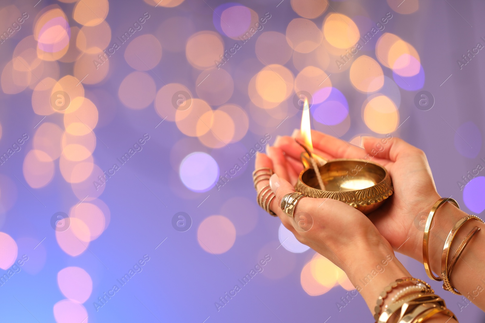 Photo of Diwali celebration. Woman holding lit diya lamp on color background with blurred lights, closeup. Space for text