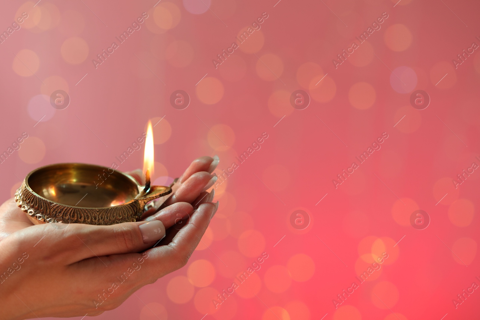 Photo of Diwali celebration. Woman holding lit diya lamp on color background with blurred lights, closeup. Space for text