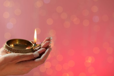 Diwali celebration. Woman holding lit diya lamp on color background with blurred lights, closeup. Space for text