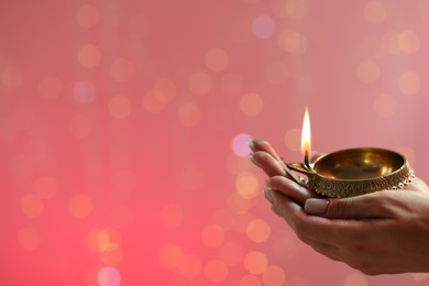 Diwali celebration. Woman holding lit diya lamp on color background with blurred lights, closeup. Space for text