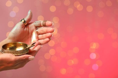 Photo of Diwali celebration. Woman holding lit diya lamp on color background with blurred lights, closeup. Space for text