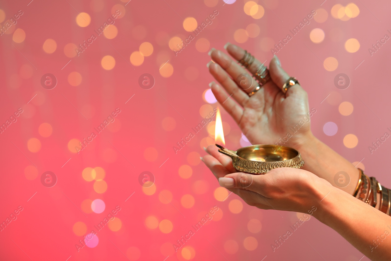 Photo of Diwali celebration. Woman holding lit diya lamp on color background with blurred lights, closeup. Space for text