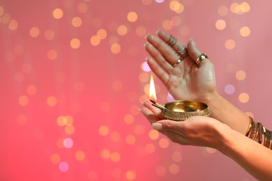 Photo of Diwali celebration. Woman holding lit diya lamp on color background with blurred lights, closeup. Space for text