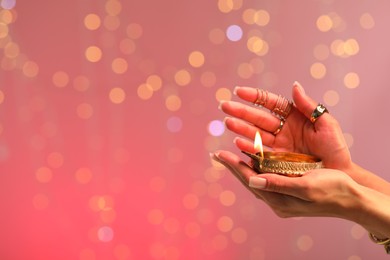 Photo of Diwali celebration. Woman holding lit diya lamp on color background with blurred lights, closeup. Space for text