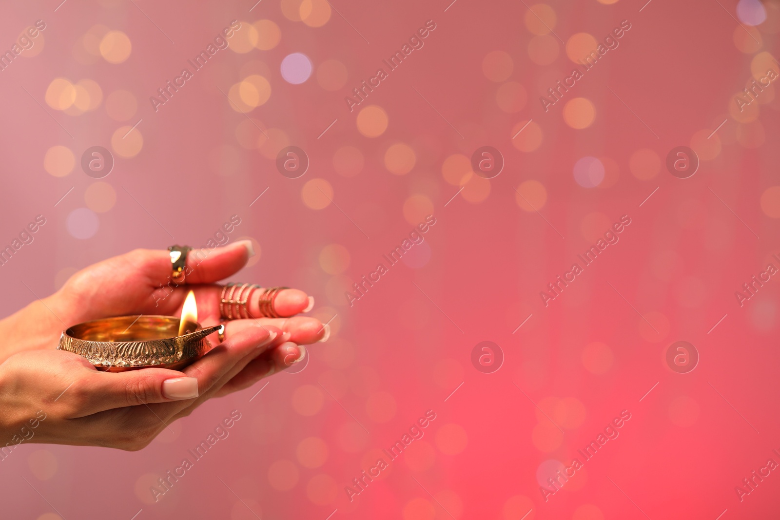 Photo of Diwali celebration. Woman holding lit diya lamp on color background with blurred lights, closeup. Space for text