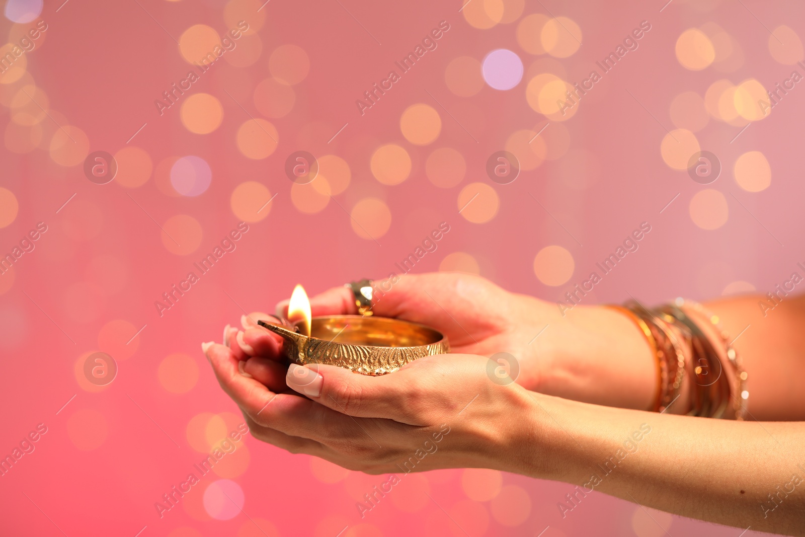 Photo of Diwali celebration. Woman holding lit diya lamp on color background with blurred lights, closeup