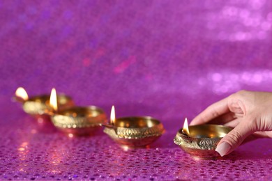 Photo of Diwali celebration. Woman with lit diya lamp on pink background, closeup