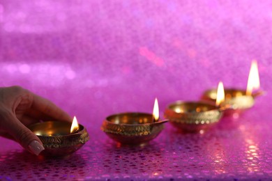 Photo of Diwali celebration. Woman with lit diya lamp on pink background, closeup