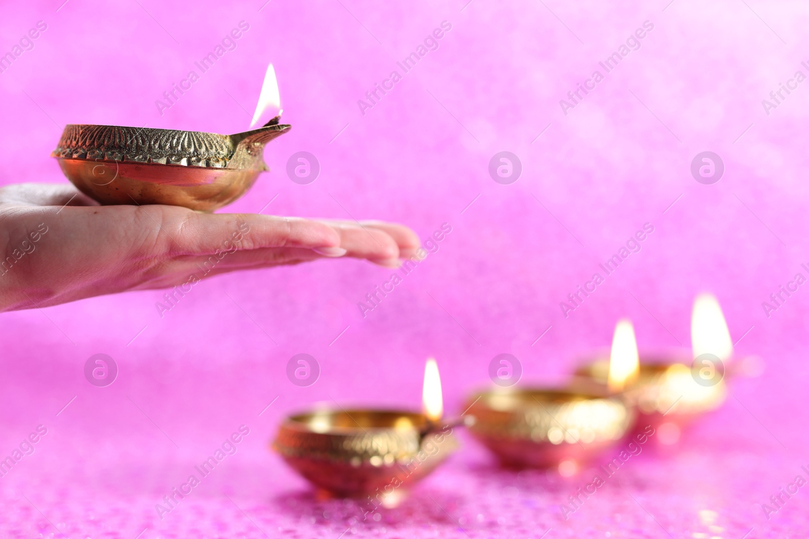 Photo of Diwali celebration. Woman holding lit diya lamp on pink background, closeup