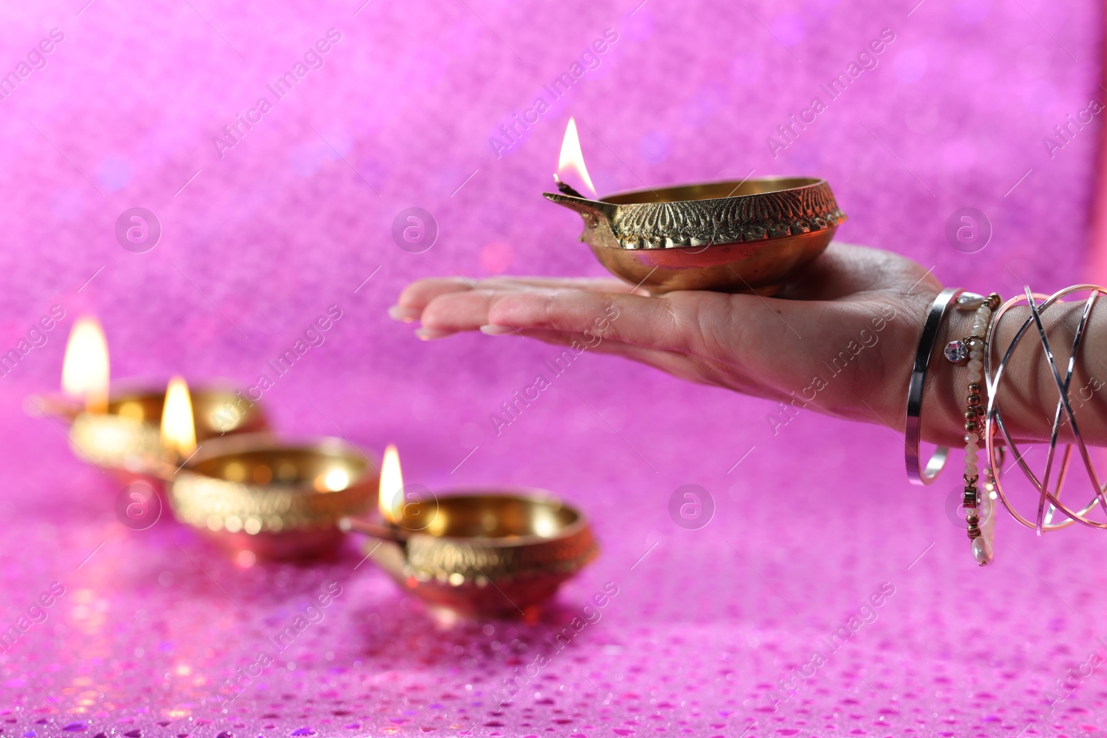 Photo of Diwali celebration. Woman holding lit diya lamp on pink background, closeup