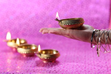 Photo of Diwali celebration. Woman holding lit diya lamp on pink background, closeup