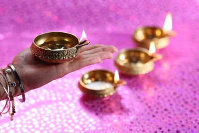 Photo of Diwali celebration. Woman holding lit diya lamp on pink background, closeup