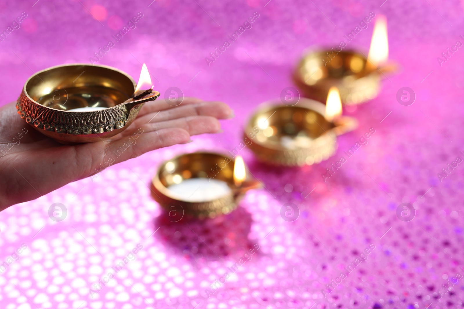 Photo of Diwali celebration. Woman holding lit diya lamp on pink background, closeup