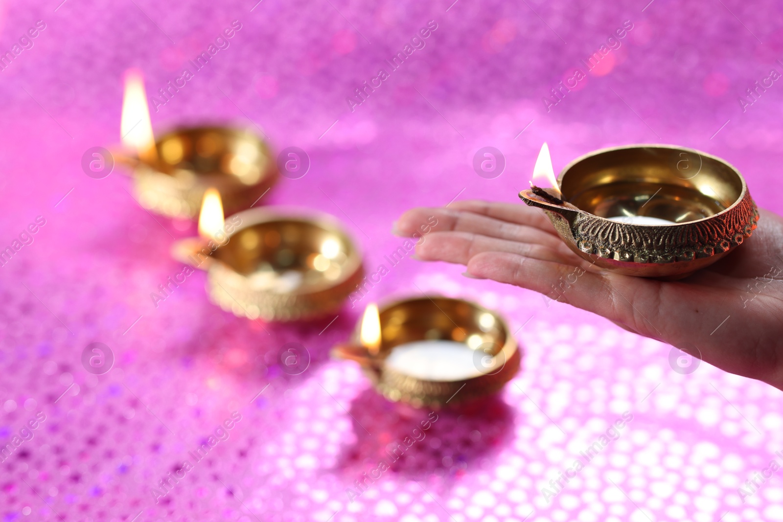 Photo of Diwali celebration. Woman holding lit diya lamp on pink background, closeup