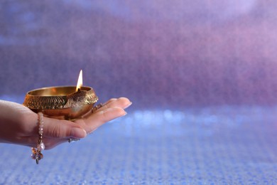 Photo of Diwali celebration. Woman holding lit diya lamp on color background, closeup. Space for text